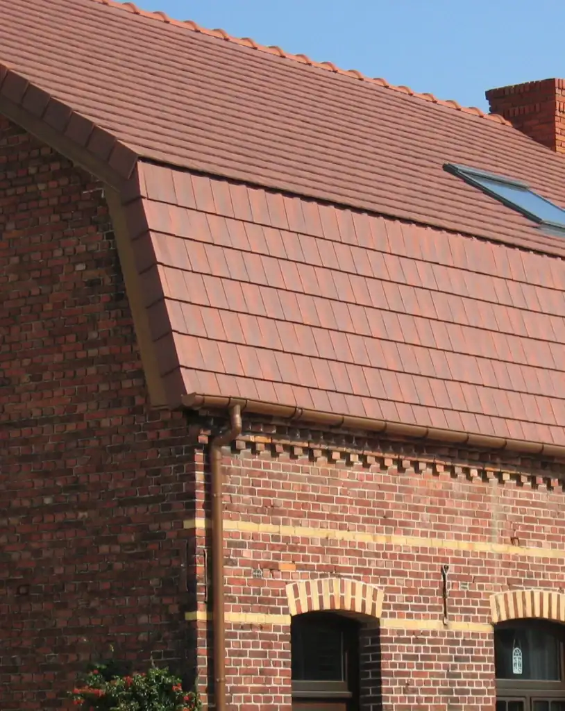 Brick house roofed with red Edilians flat tiles under clear blue sky