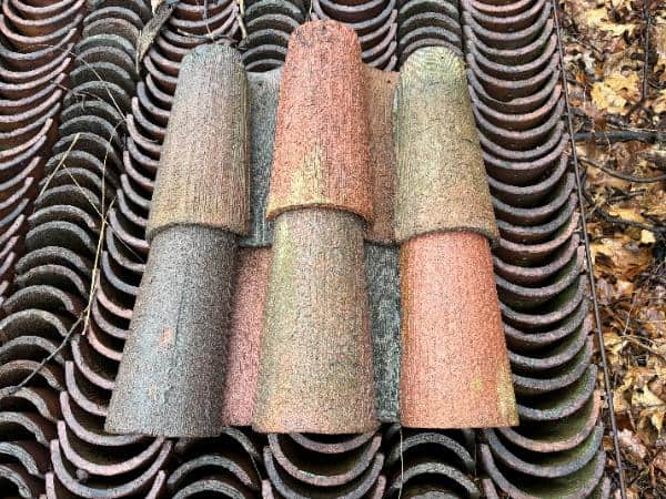 Stack of reclaimed barrel clay roof tiles in red, brown, and moss-weathered finishes, showing natural aging and curved mission profile