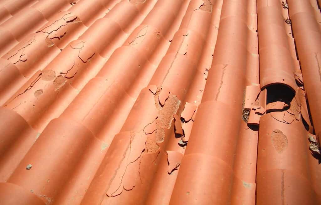 Clay roof tiles showing severe delamination and surface failure caused by moisture absorption and freeze-thaw damage.