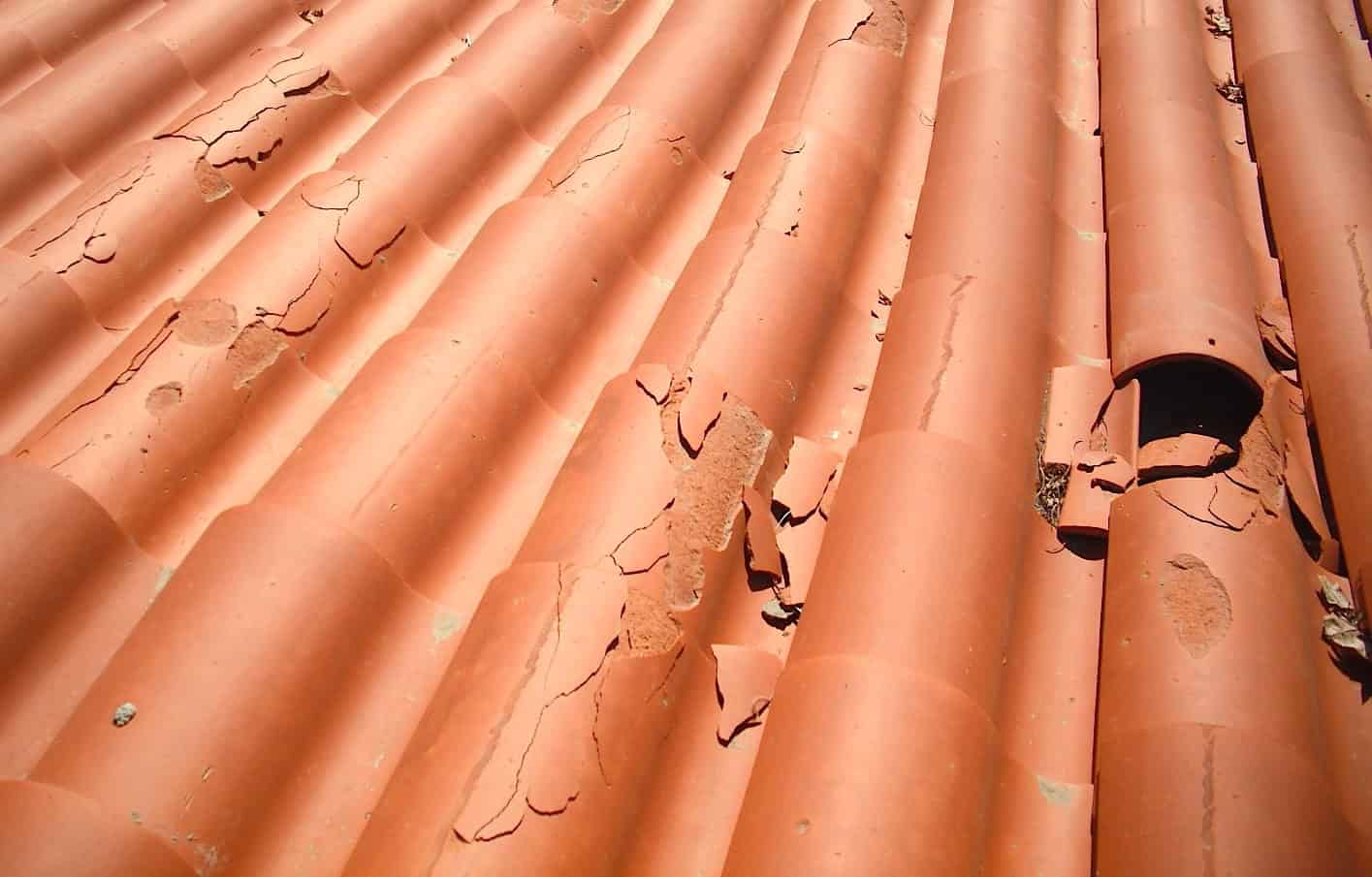 Clay roof tiles showing severe delamination and surface failure caused by moisture absorption and freeze-thaw damage.