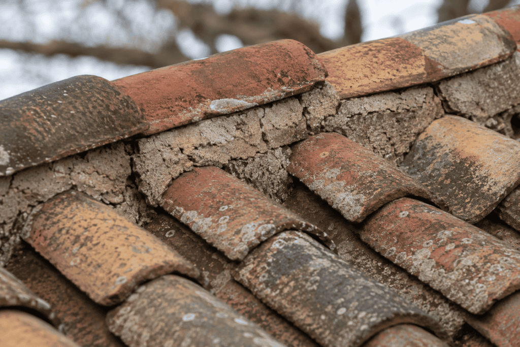 Close-up of weathered reclaimed clay roof tiles with cracked aging ridge mortar on an older historic roof